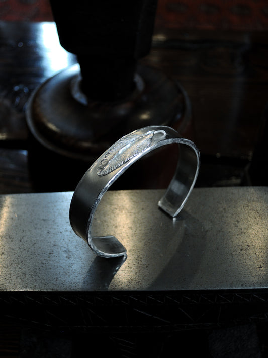 A hand made sterling silver cuff made using repousse and chasing technique. A feather is placed at the center.