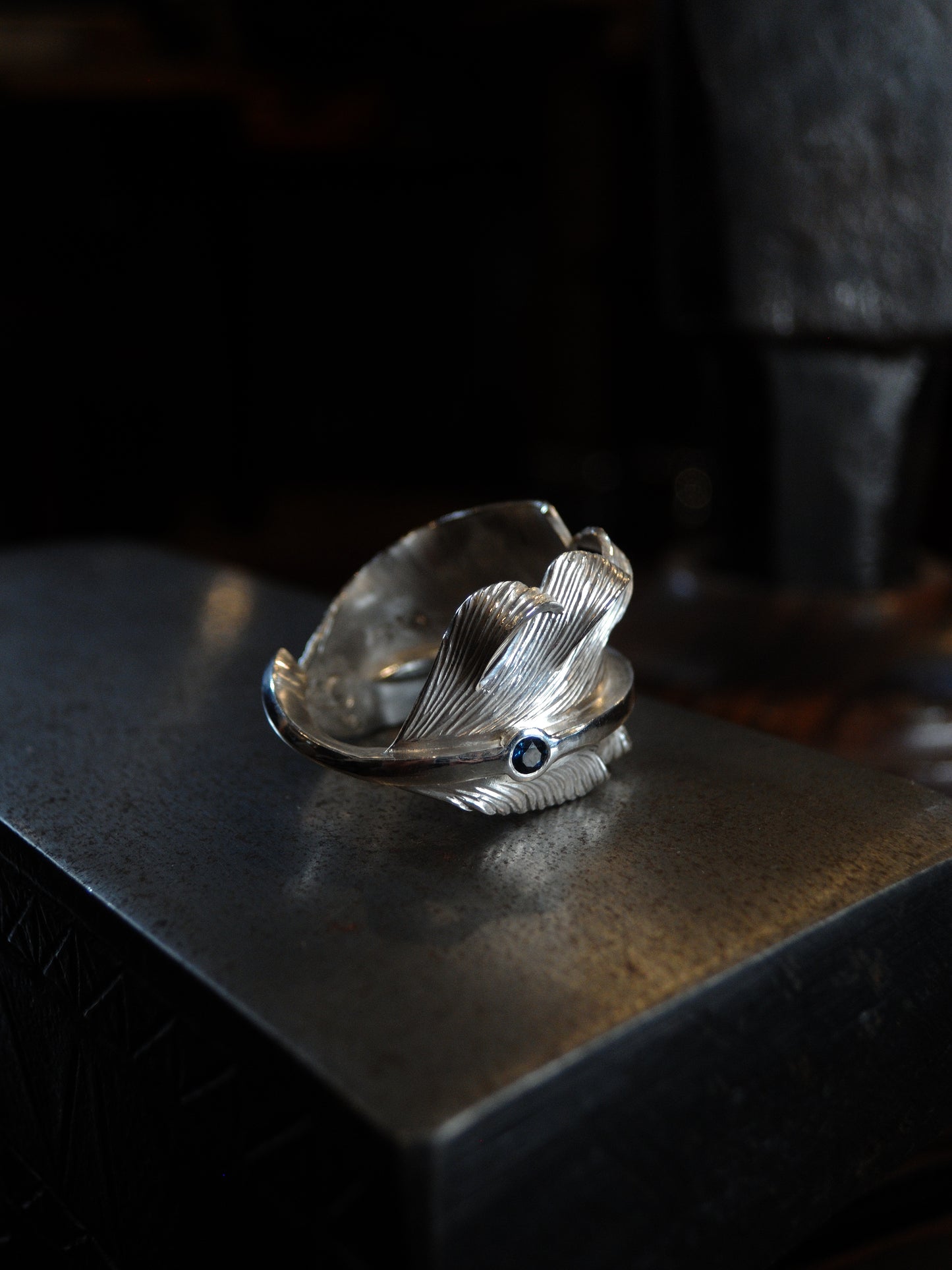 A sterling silver feather ring made using traditional repousse and chasing techniques. It is set with a blue sapphire.