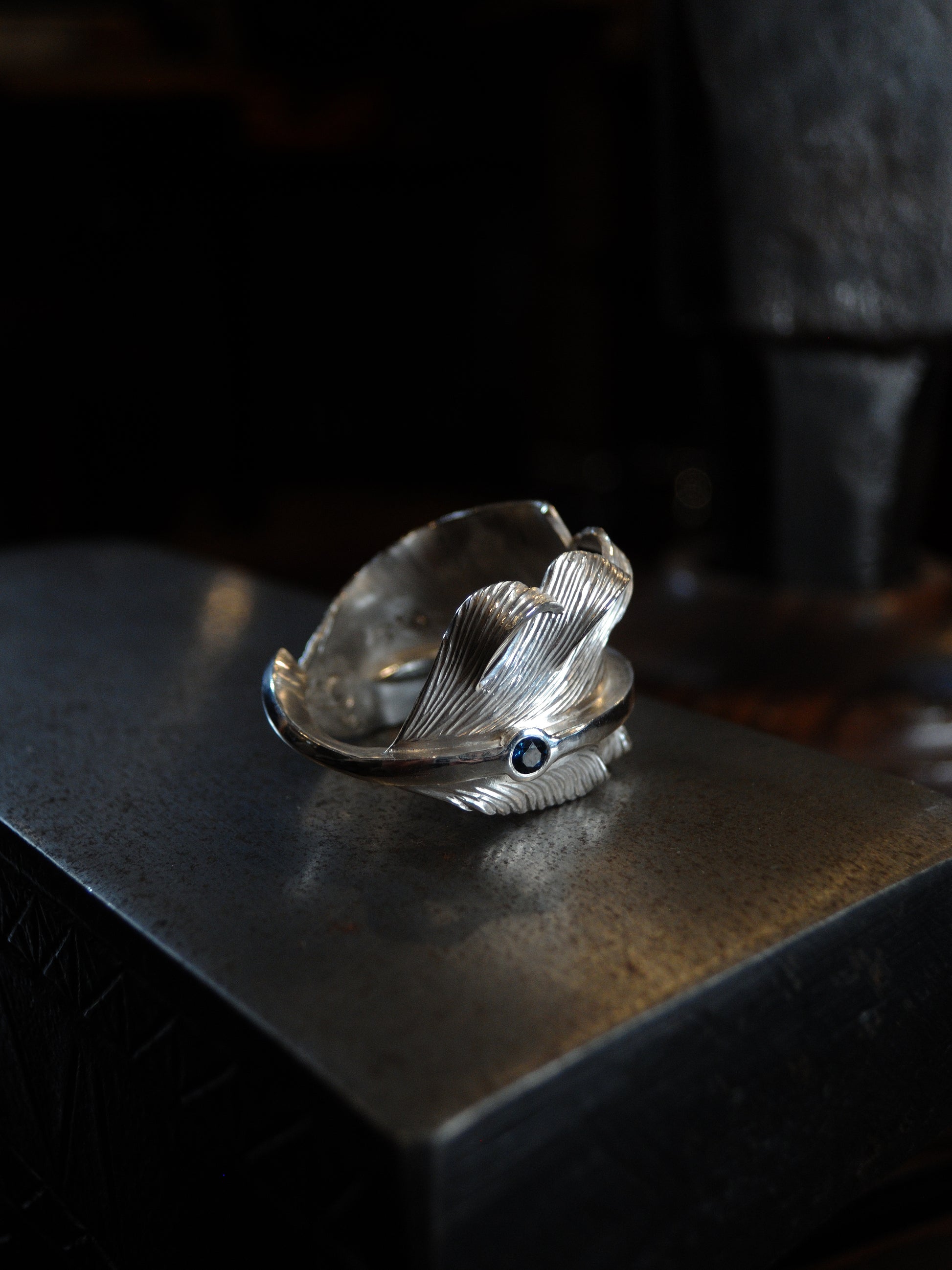 A sterling silver feather ring made using traditional repousse and chasing techniques. It is set with a blue sapphire.