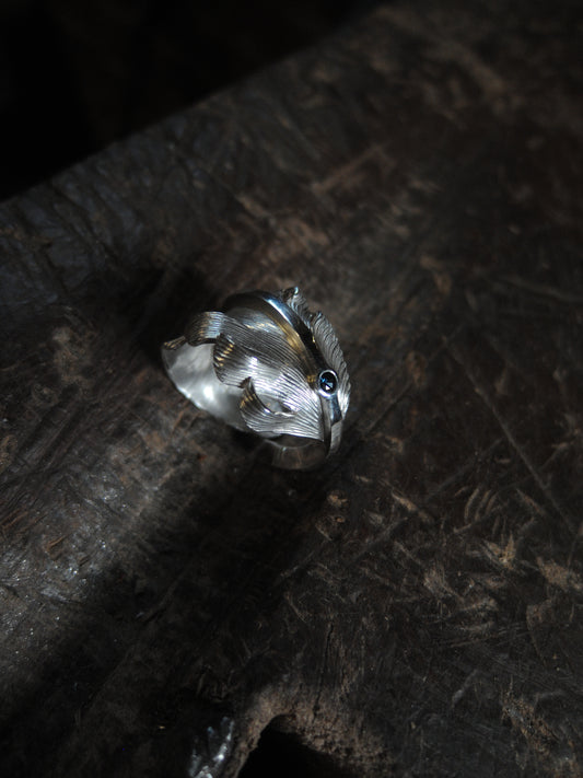 A sterling silver feather ring made using traditional repousse and chasing techniques. It is set with a blue sapphire.