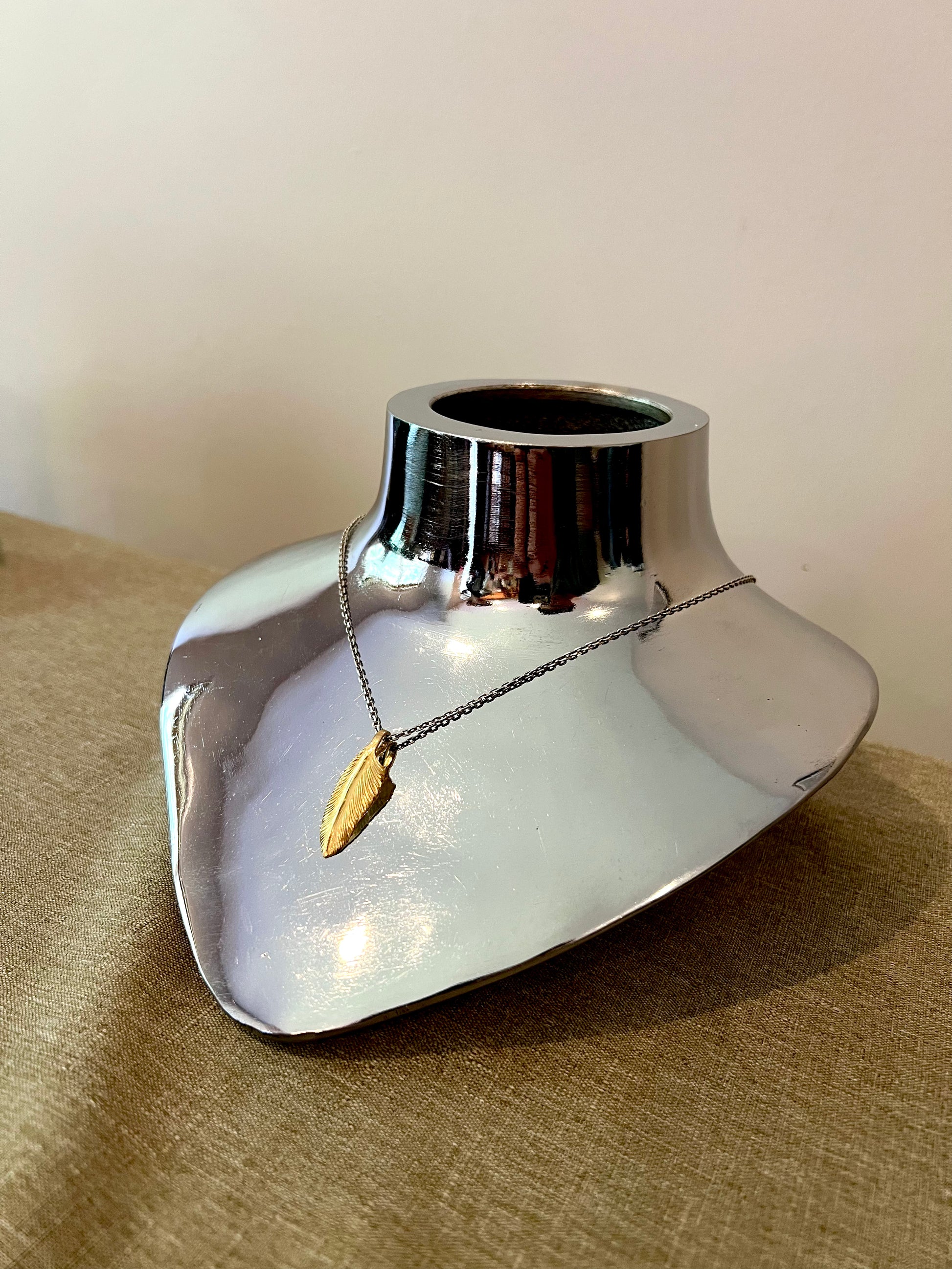A 22k gold feather charm displayed on a mannequin.